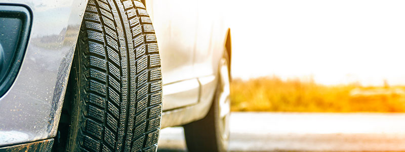 Close-up of a grey car’s front tire against a bright, sunlit background.
